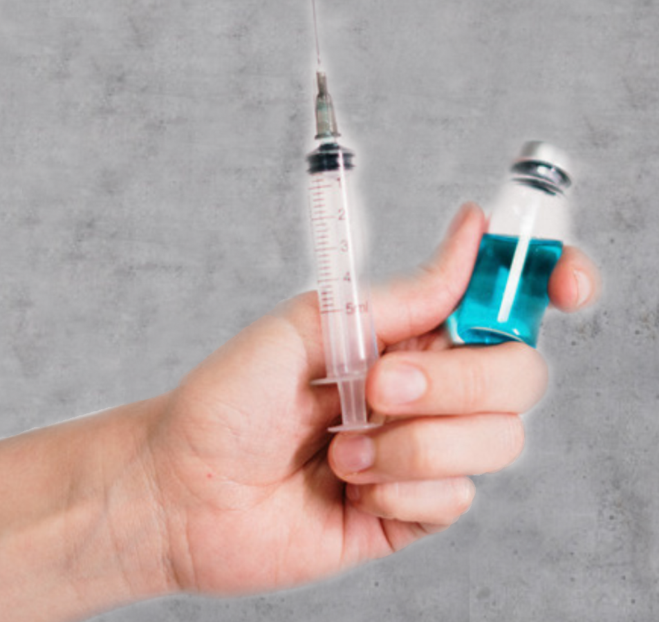 Hand hält eine gefüllte Spritze und ein Impf-Fläschchen mit blauer Flüssigkeit vor grauem Hintergrund.