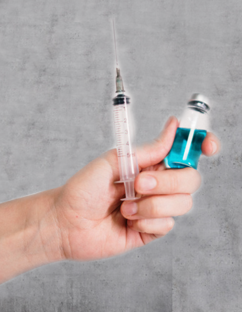 Hand hält eine gefüllte Spritze und ein Impf-Fläschchen mit blauer Flüssigkeit vor grauem Hintergrund.