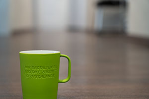 Grüne Kaffeetasse im Münchener Office mit der Aufschrift "Wir gestalten die digitale Zukunft Deutschlands".