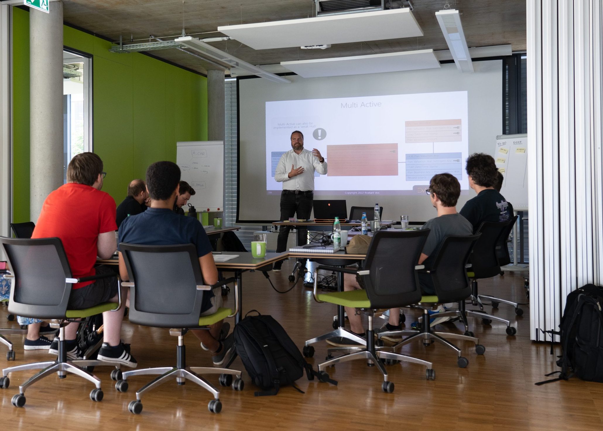Roelant Vos holds a training session in front of a group of employees in a modern seminar room.