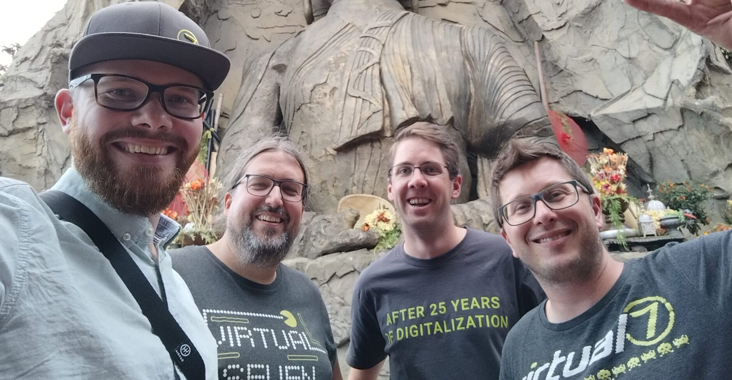 Four virtual7 employees laughing into the camera in front of a detailed stone wall in an amusement park.