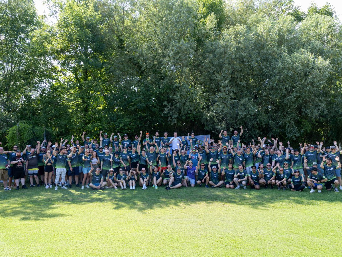 Großes Gruppenfoto der virtual7 conference 2025 mit zahlreichen Mitarbeitenden in grünen virtual7-Shirts, die gemeinsam im Freien feiern und jubeln.