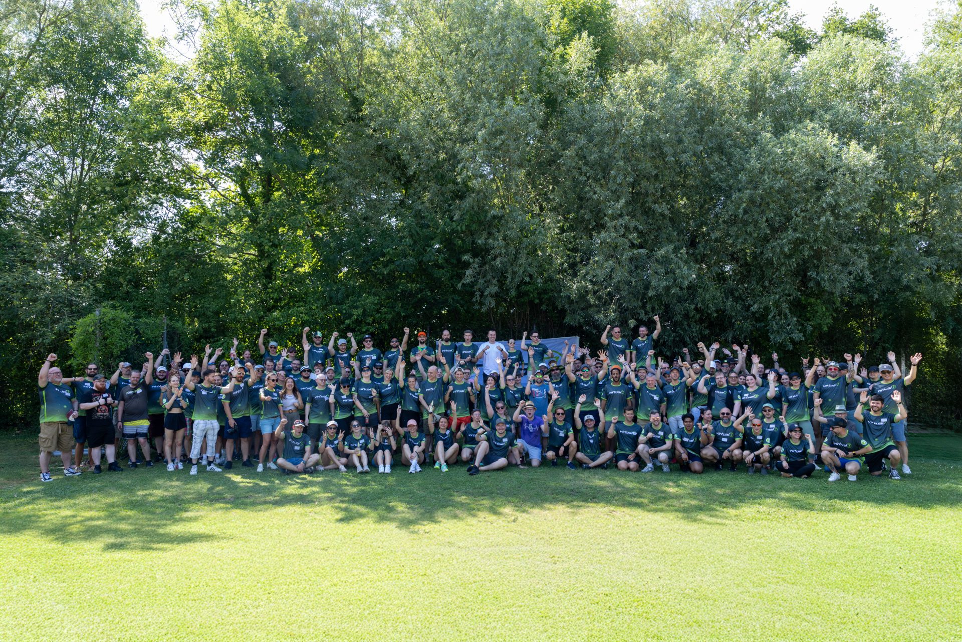 Großes Gruppenfoto der virtual7 conference 2025 mit zahlreichen Mitarbeitenden in grünen virtual7-Shirts, die gemeinsam im Freien feiern und jubeln.