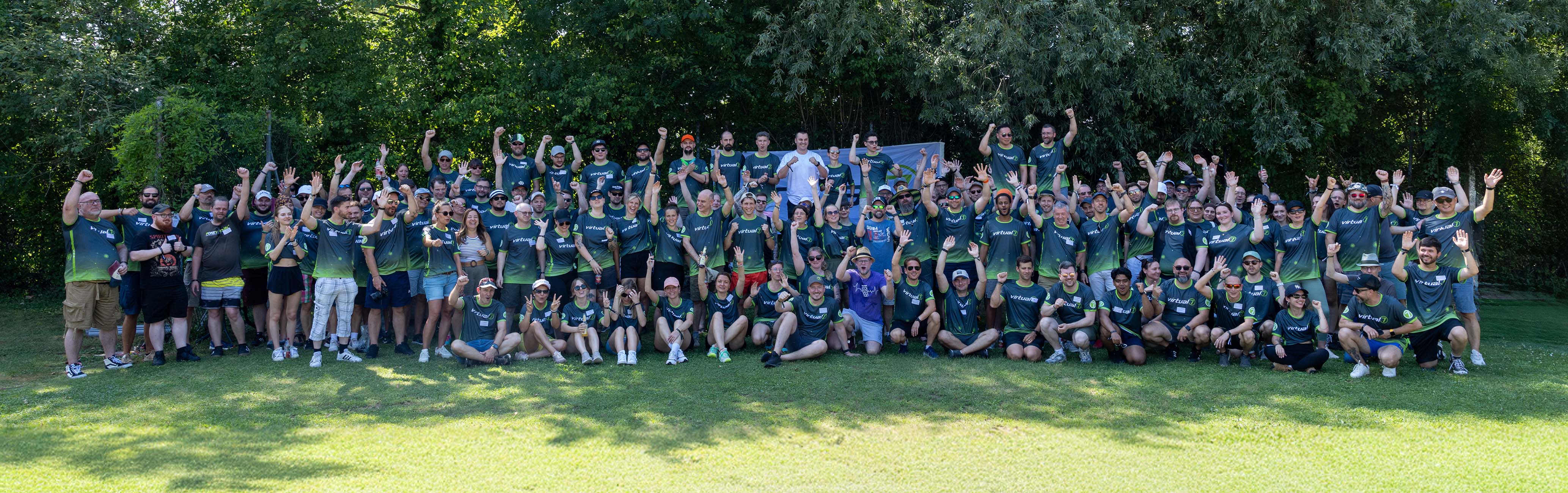 Gruppenfoto der virtual7 conference 2025 mit zahlreichen Mitarbeitenden in grünen und schwarzen virtual7-Shirts, die gemeinsam im Freien feiern und jubeln.